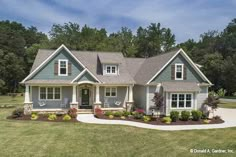 a large blue house in the middle of a grassy area with lots of trees and bushes