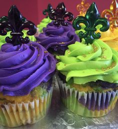 three cupcakes with purple, green and yellow frosting are on a table