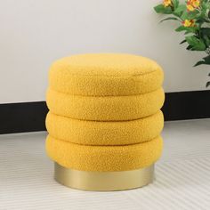 a stack of yellow towels sitting on top of a round metal stand next to a potted plant