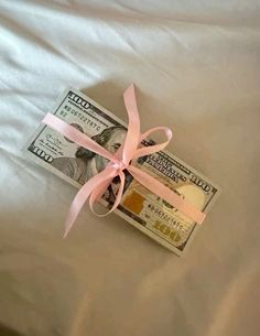 a bundle of money tied to a pink ribbon on top of a white bed sheet