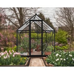 a small greenhouse in the middle of a garden with lots of flowers and plants around it