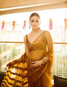 a woman in an orange and yellow sari posing for the camera with her hand on her hip