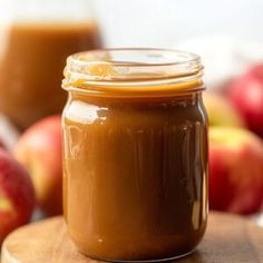 a jar of peanut butter sitting on top of a wooden table next to some apples