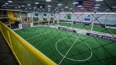 an indoor soccer field with green grass and yellow goal posts in the center, surrounded by lights