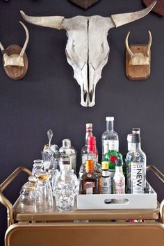 a bar cart with bottles and glasses on it in front of a wall mounted bull skull