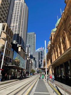 people are walking down the street in front of tall buildings and skyscrapers on a sunny day