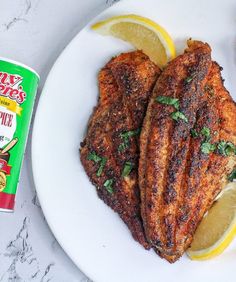 two pieces of chicken on a plate with lemons and seasoning next to it