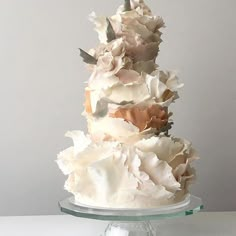 a three tiered cake with white frosting and flowers on the top is sitting on a glass platter