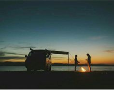 two people standing next to a camper van at sunset