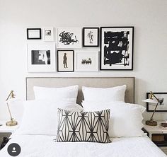 a bed with white sheets, pillows and pictures on the wall