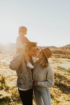 a man holding a baby up to his face while standing next to a woman in a field