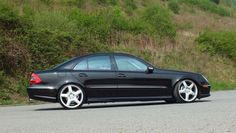 a black car parked on the side of a road next to a lush green hillside