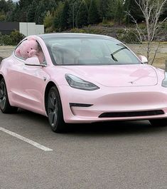 a pink car parked in a parking lot with a teddy bear sticking its head out the window