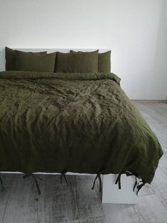 a bed with green sheets and pillows in a white walled room next to a wooden floor