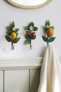 three oranges and two strawberries are hanging on the wall next to a towel rack