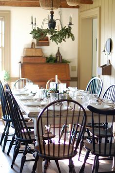 the dining room table is set with white plates and black chairs, along with greenery hanging from the chandelier