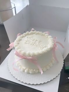 a white cake sitting on top of a table next to a box with pink ribbon