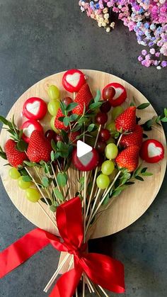 strawberries, grapes and apples arranged on a wooden plate with red ribbon tied around it