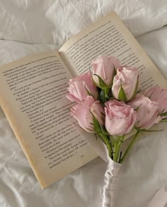 a bouquet of pink flowers sitting next to an open book on top of a bed