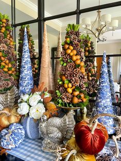 a table topped with blue and white vases filled with oranges, pine cones and pumpkins