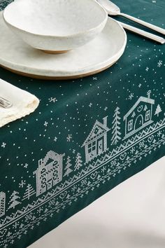 a green table cloth with white snowflakes and houses on it is next to a plate