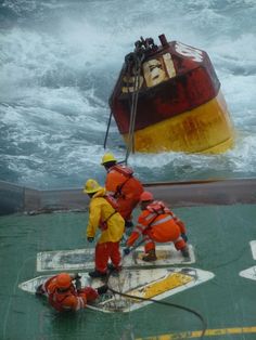 two men in orange and yellow work on the side of a boat