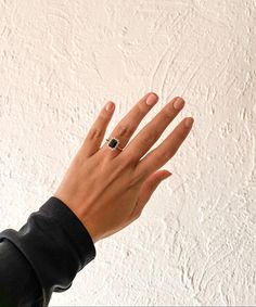 a person's hand with a ring on it and a white wall in the background