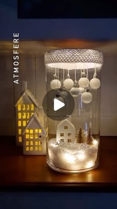 a glass jar filled with snow and christmas ornaments on top of a table next to a house