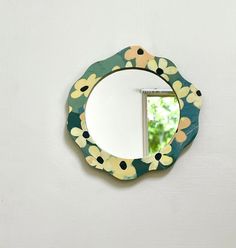 a round mirror mounted to the side of a wall with flowers on it and a small window