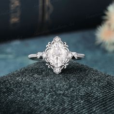 a white diamond ring sitting on top of a black velvet surface with flowers in the background