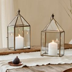 two glass lanterns sitting on top of a wooden table next to a white towel and candle