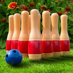 several wooden bowling pins lined up next to a blue ball on the grass with flowers in the background