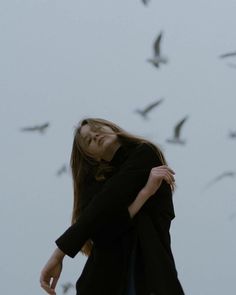 a woman standing in front of a flock of birds with her eyes closed and head tilted to the side