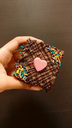 a hand holding a piece of chocolate covered in sprinkles and a heart