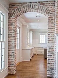 an empty room with wood flooring and brick arches on the wall, along with windows