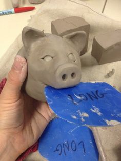 a hand holding a clay pig head next to a piece of blue paper with the word love on it