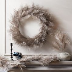 a silver wreath and two candles on a mantle with white walls in the back ground