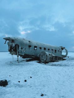 an old airplane sitting in the middle of nowhere on snow covered ground with rocks around it