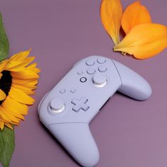 a close up of a nintendo wii controller next to a sunflower on a purple surface