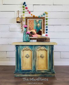 an old dresser painted blue and yellow with pom poms on the wall behind it