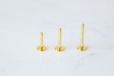 three pairs of gold - plated ear posts on a white marble surface, with one in the foreground