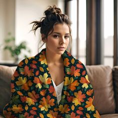 a woman sitting on top of a couch covered in a colorful fall leaf print blanket