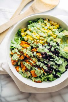 a white bowl filled with black beans, corn and guacamole dressing on top of lettuce