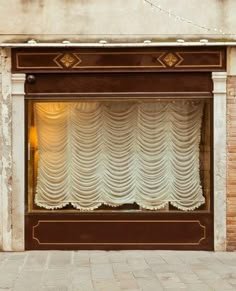 a storefront with curtains and lights on the side walk in front of an old brick building