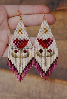 a pair of beaded earrings with red and white flowers hanging from it's sides