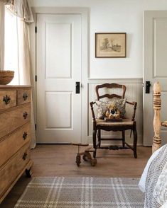 a bedroom with white walls and wooden furniture in the corner, along with a teddy bear sitting on an old chair