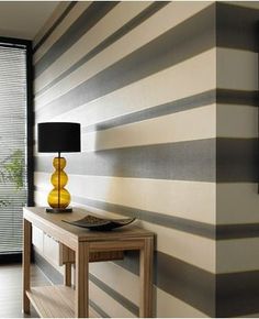 a living room with striped wallpaper and a yellow vase on a table in front of a sliding glass door