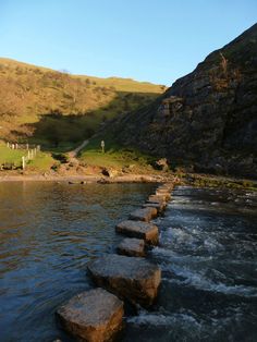 stepping stones in the middle of a body of water next to a grassy hill side