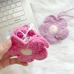 a hand holding a small pink crocheted object next to a keyboard