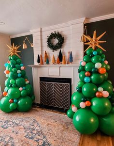 two green christmas trees in front of a fireplace with gold stars on top and balloons around them